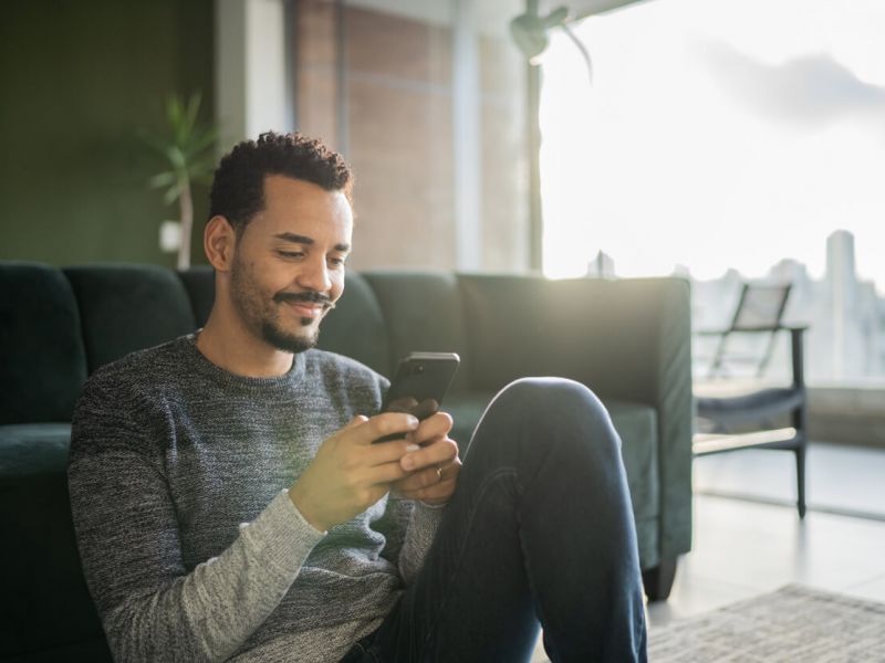 Man sitting in living room using is smartphone to order cannabis online in pahrump with the skyline in background