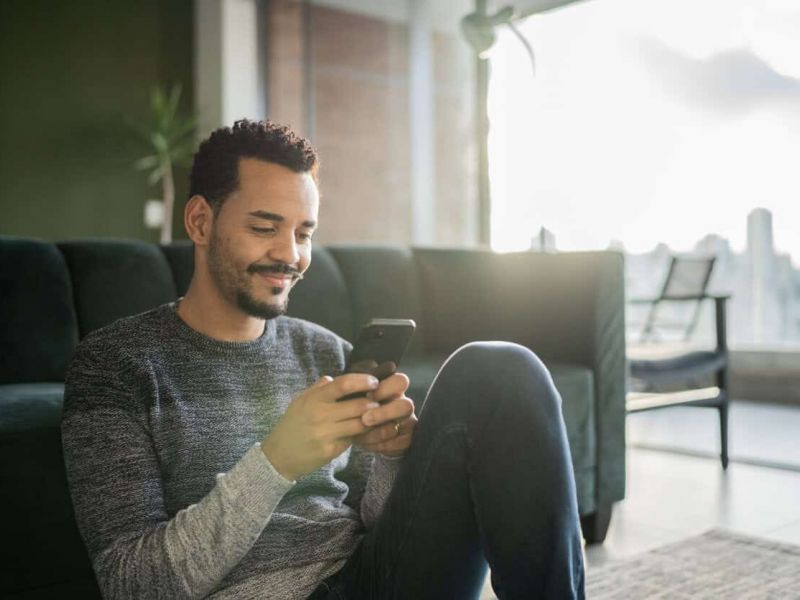 Man sitting in living room using is smartphone to order cannabis online in pahrump with the skyline in background